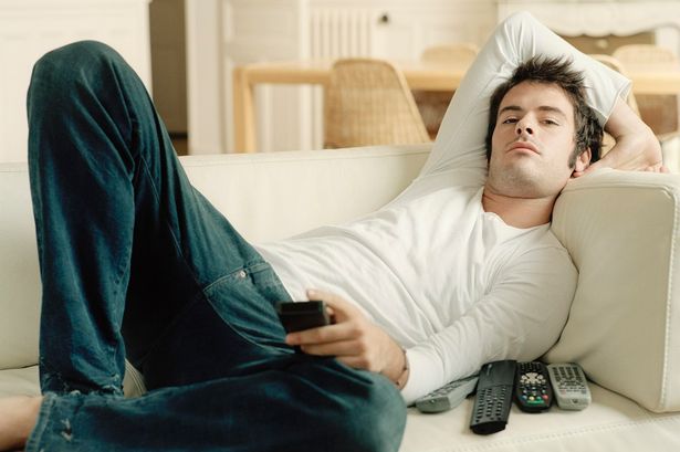 Man relaxing on sofa holding remote controls-189729