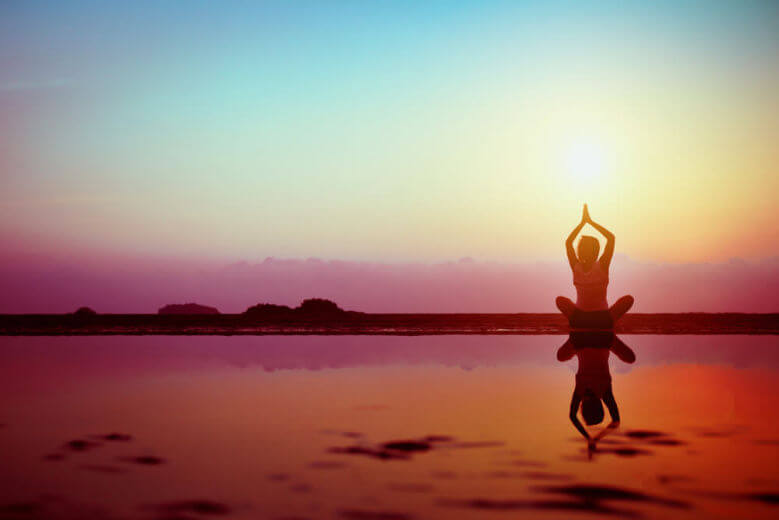 Silhouette of young woman practicing yoga on the beach at sunset