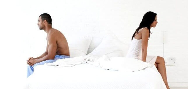Man and women sitting on opposite sides of bed with backs facing each other