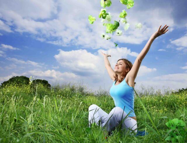 Happy woman sitting cross-legged in field throwing leaves into the air
