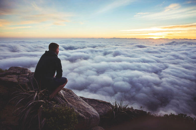 Man sitting on cliff looking out over clouds 