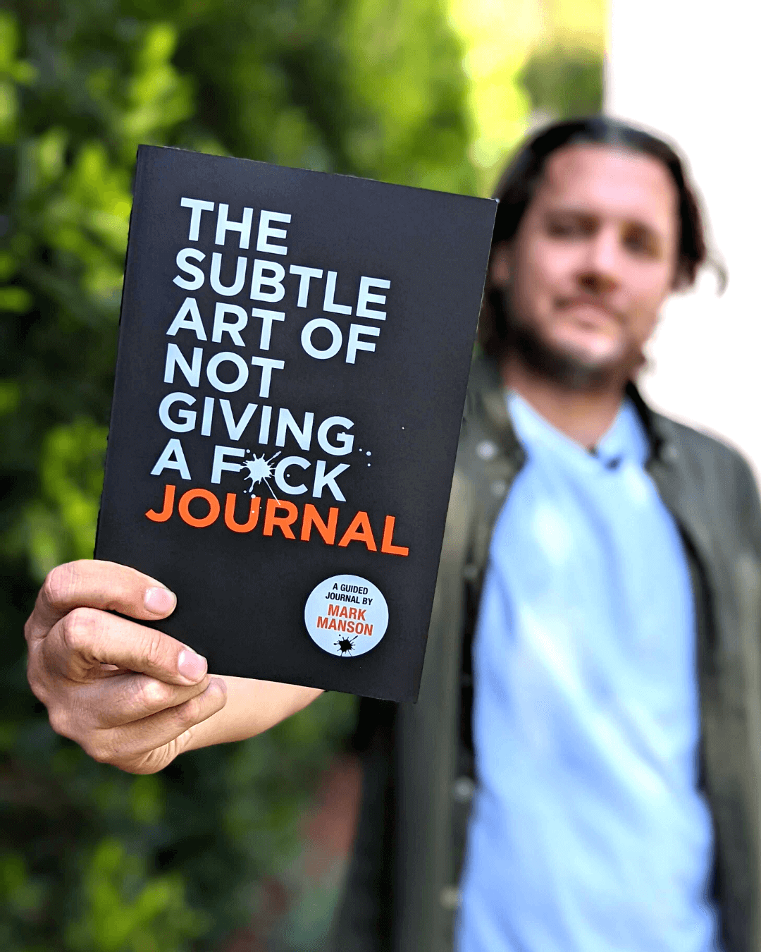 Mark Manson holding a copy of The Subtle Art of Not Giving a F*ck Journal